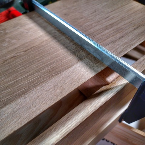 Holzbretter in Nahaufnahme, manche sind miteinander verleimt; oben ist im Anschnitt eine Zwinge sichtbar, die die Bretter aneinander hält