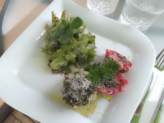 Ein Teller mit Salat, einem Spinat-Knödel und einem halbierten Rote-Beete-Knödel mit Salbei-Butter und geriebenem Parmesan, garniert mit Petersilie.